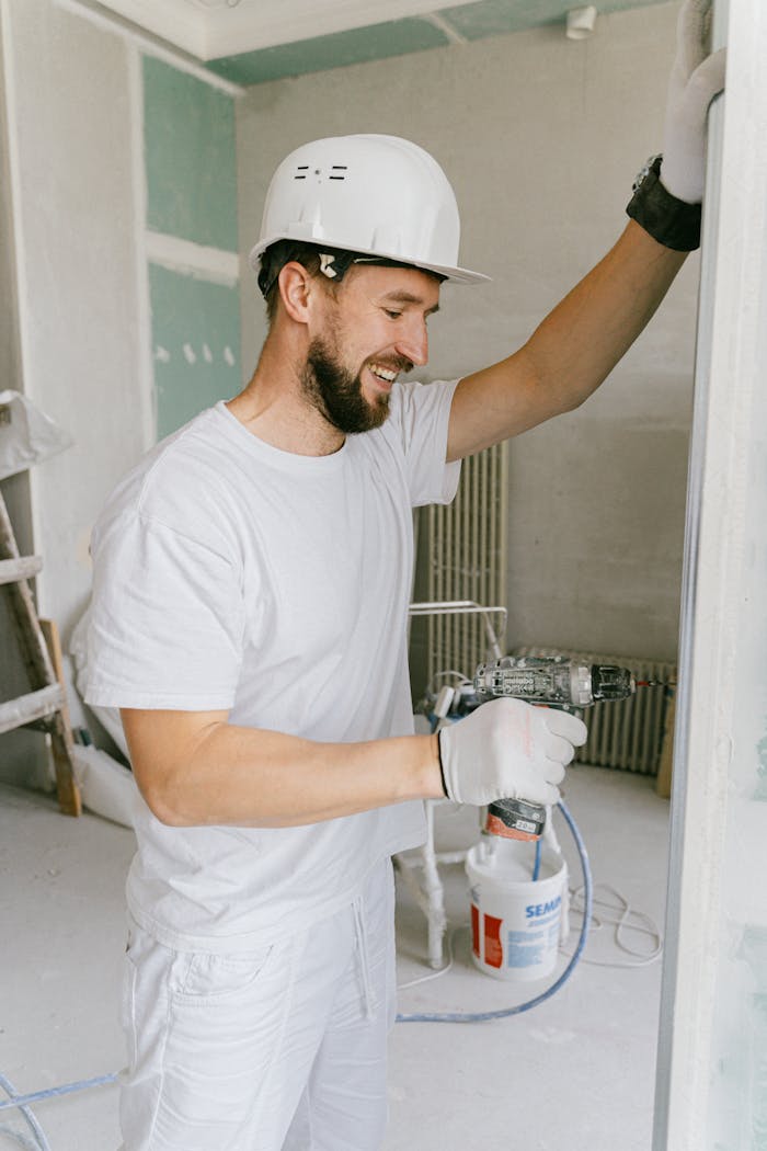 A happy construction worker using a drill indoors during renovation.