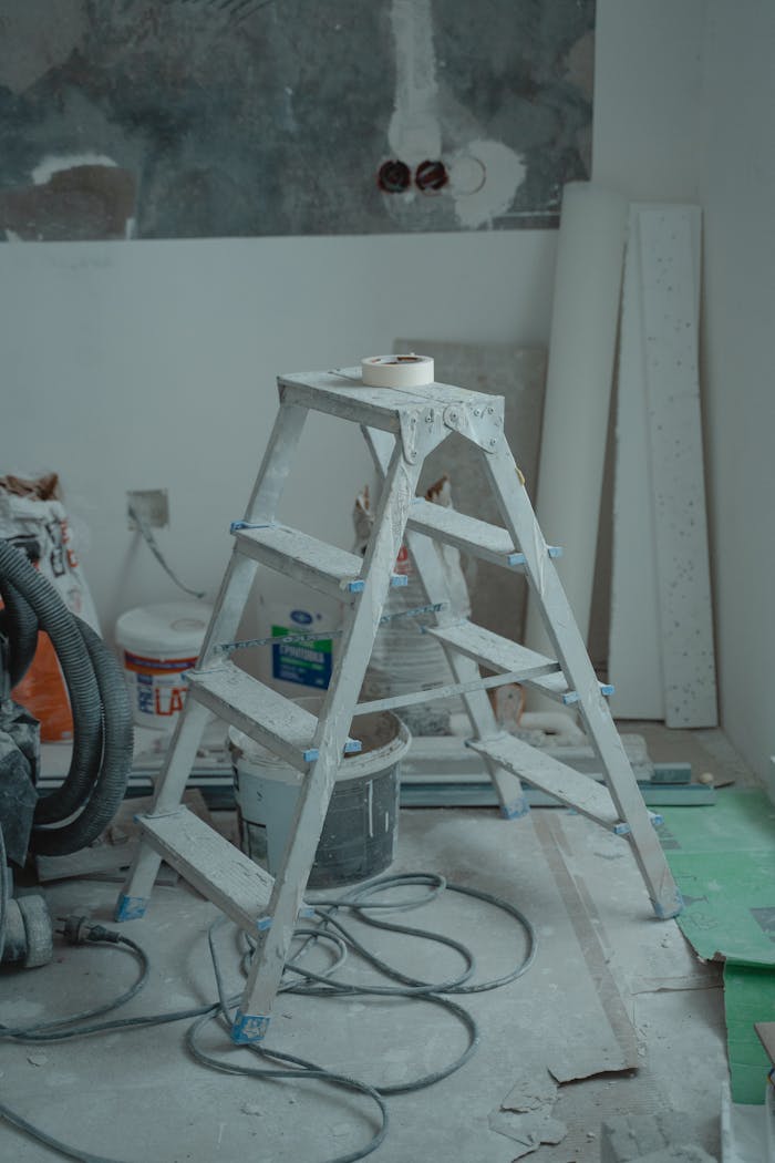 about-02 A metal ladder stands amidst renovation supplies including paints and plaster in an indoor setting.